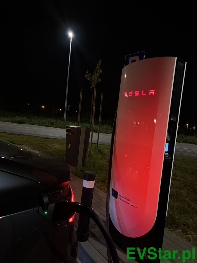 Słupek Tesla Supercharger V4 podświetlony na czerwono nocą na stacji w Gdańsku, z podpiętym kablem ładowania